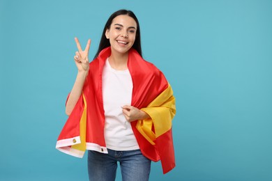 Happy young woman with flag of Spain showing V-sign on light blue background, space for text