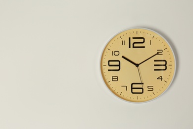 Stylish analog clock hanging on light wall. Space for text