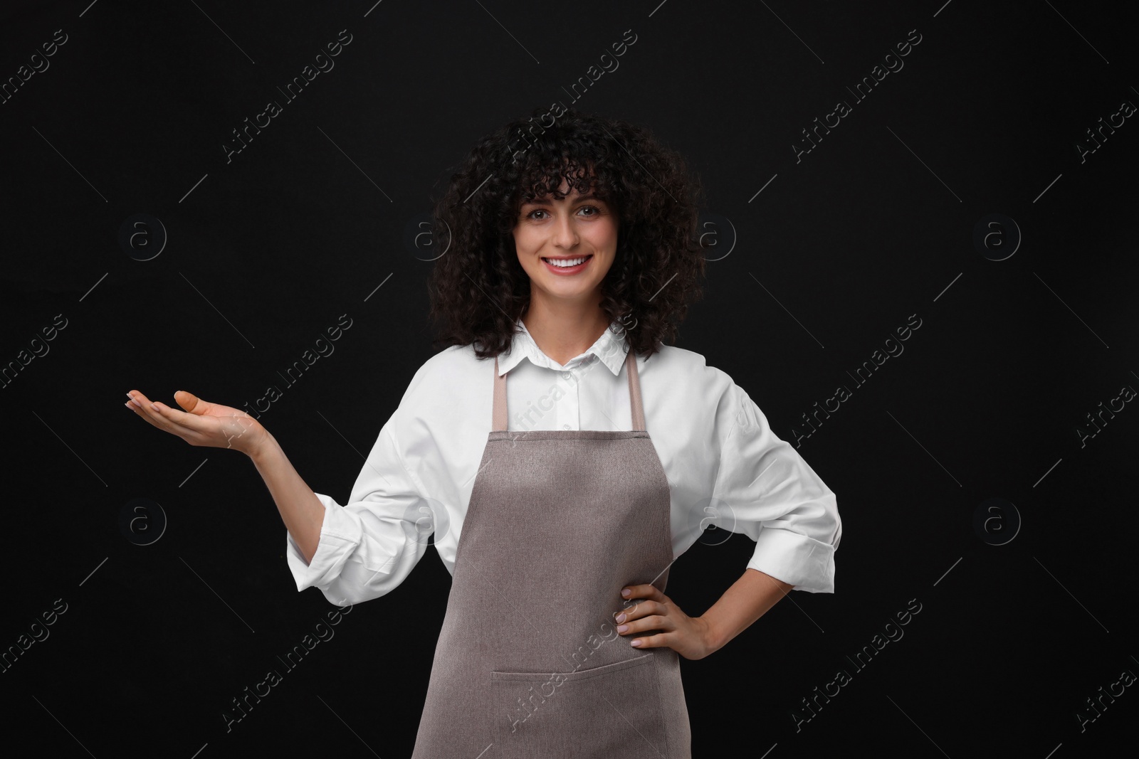 Photo of Happy woman wearing kitchen apron on black background. Mockup for design