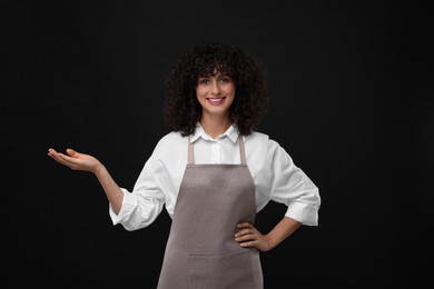 Happy woman wearing kitchen apron on black background. Mockup for design