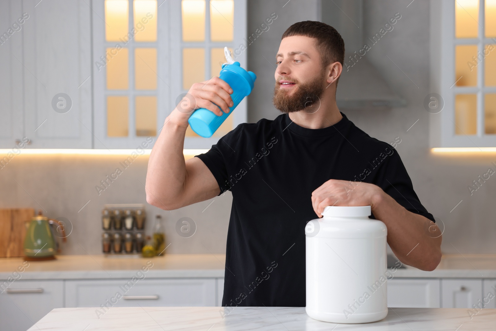 Photo of Young man with shaker of protein and powder at white marble table in kitchen