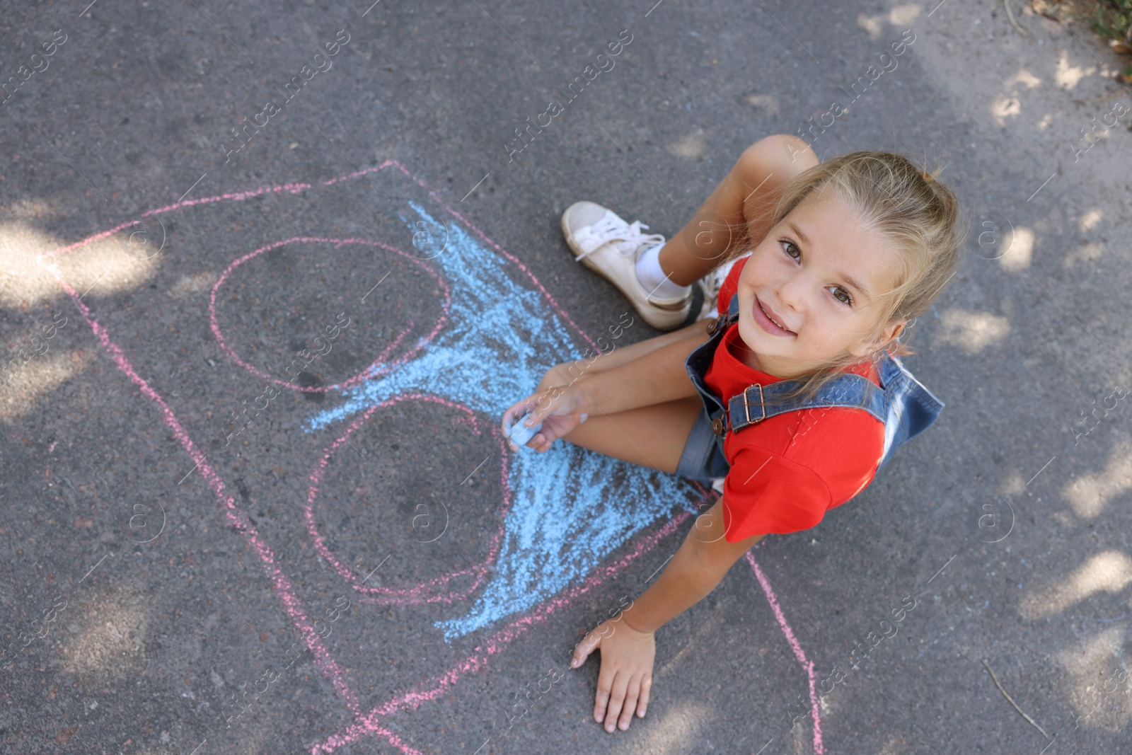 Photo of Cute little child drawing with colorful chalk on asphalt