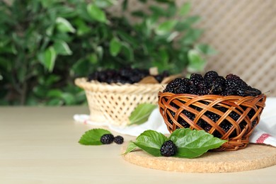 Wicker basket of delicious ripe black mulberries on white table, space for text