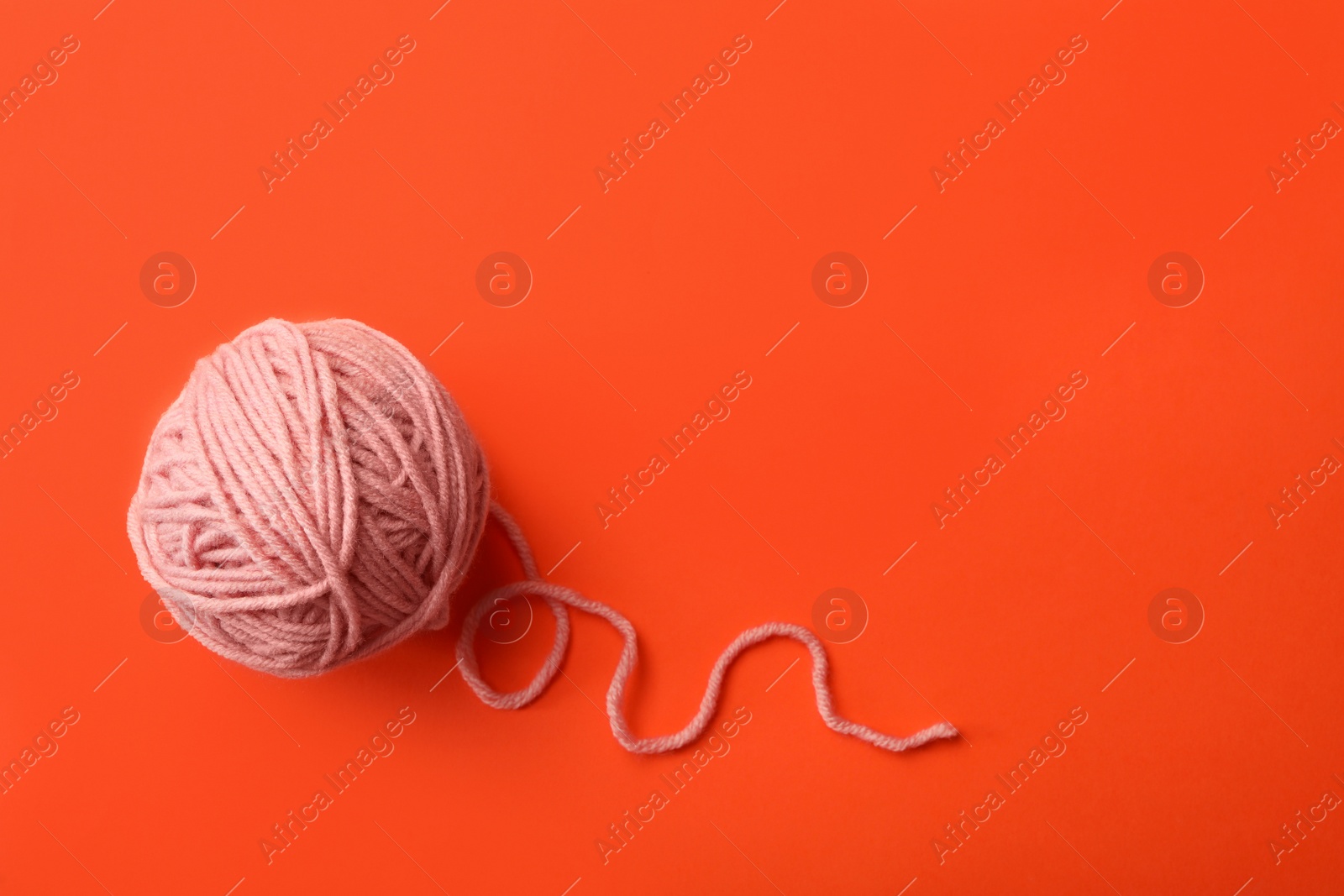 Photo of Soft pink woolen yarn on orange background, top view. Space for text