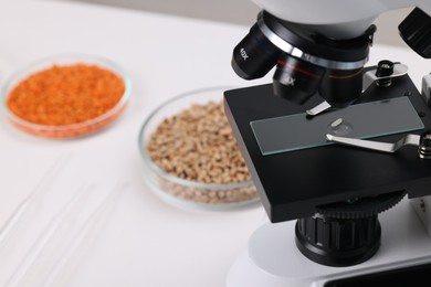 Photo of Food quality control. Glass slide with rice grain under microscope on white table, closeup