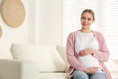 Photo of Young pregnant woman on sofa at home. Space for text