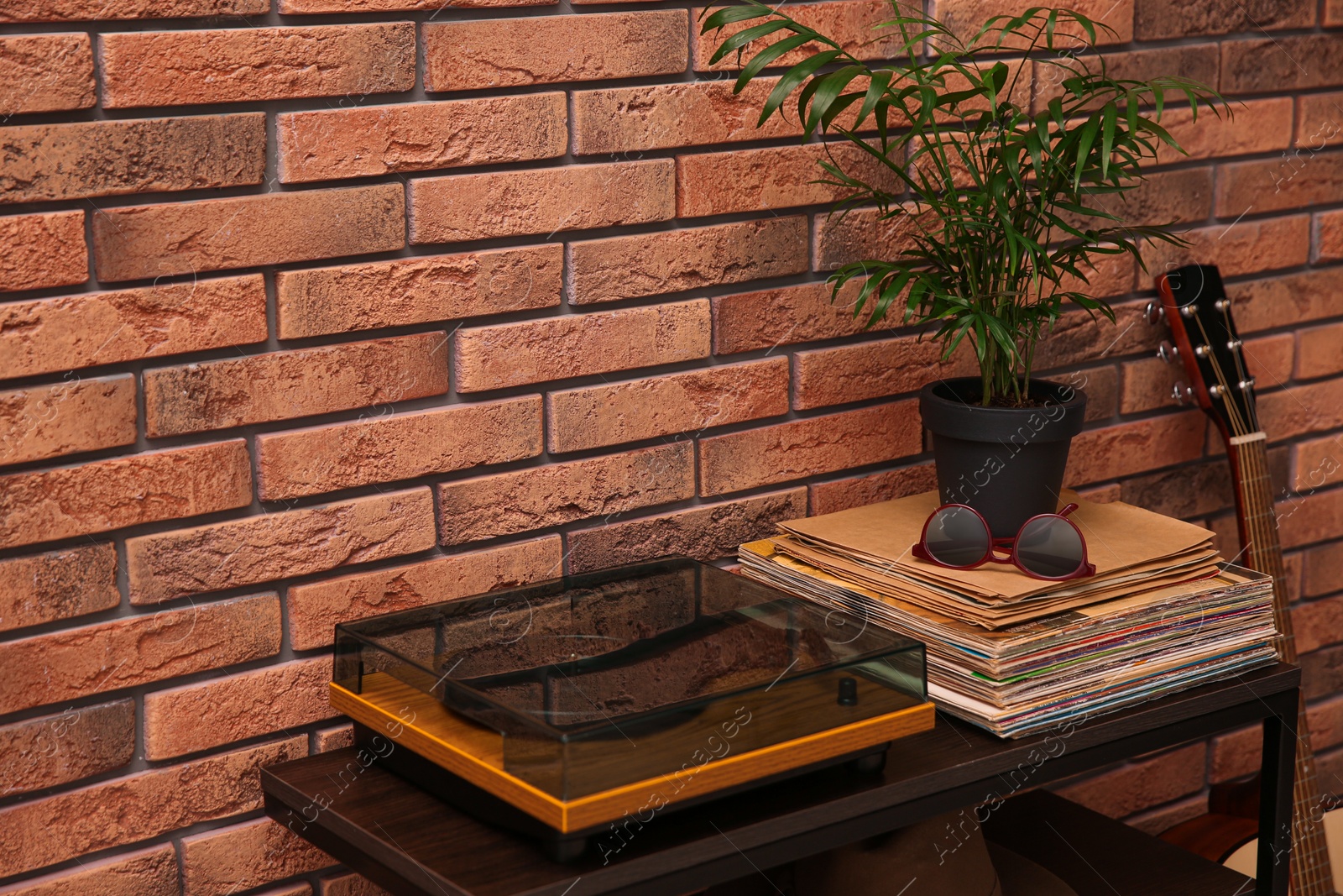 Photo of Stylish turntable and vinyl records on shelving unit near red brick wall