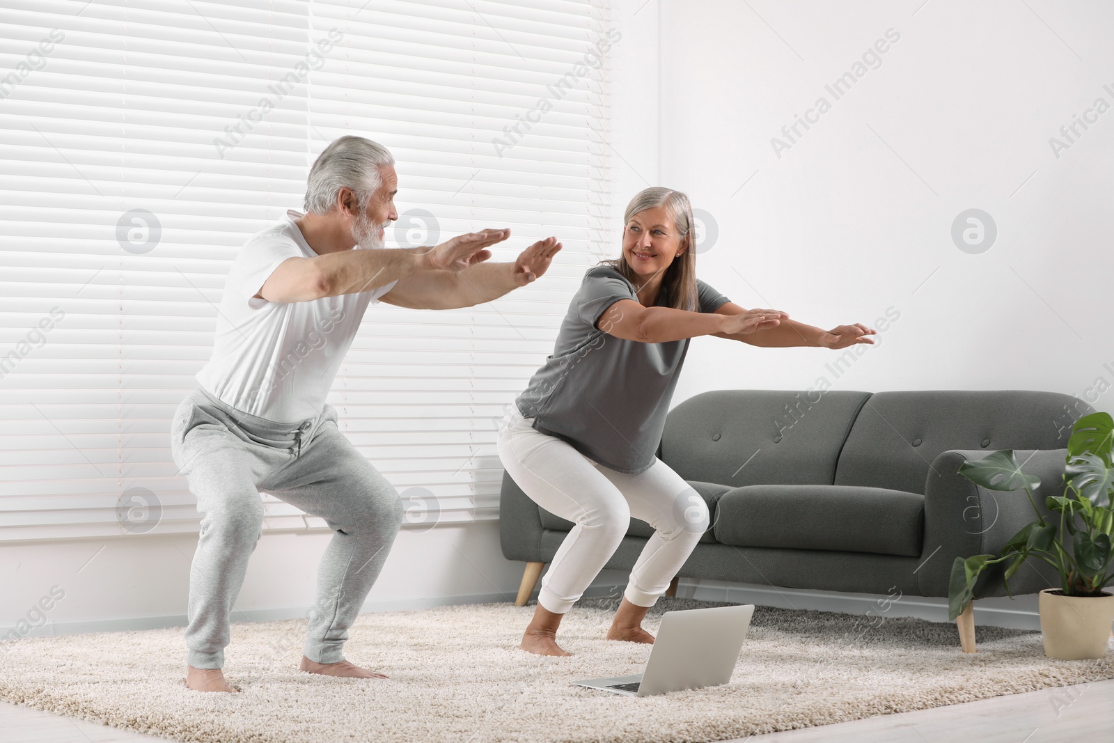 Photo of Senior couple practicing yoga with laptop on carpet at home