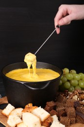 Photo of Woman dipping piece of bread into fondue pot with melted cheese at table, closeup