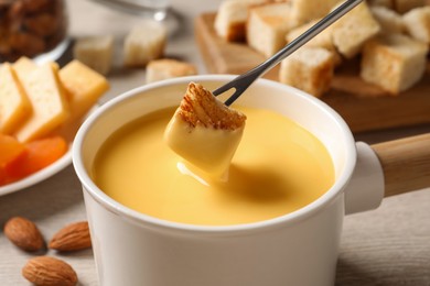 Photo of Dipping piece of bread into tasty cheese fondue at table, closeup
