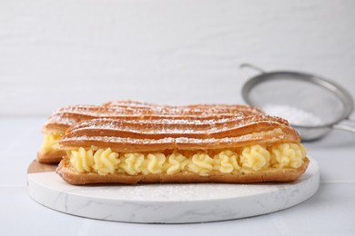 Photo of Delicious eclairs filled with cream on white table