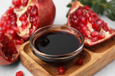 Photo of Tasty pomegranate sauce in bowl and fruits on light table, closeup