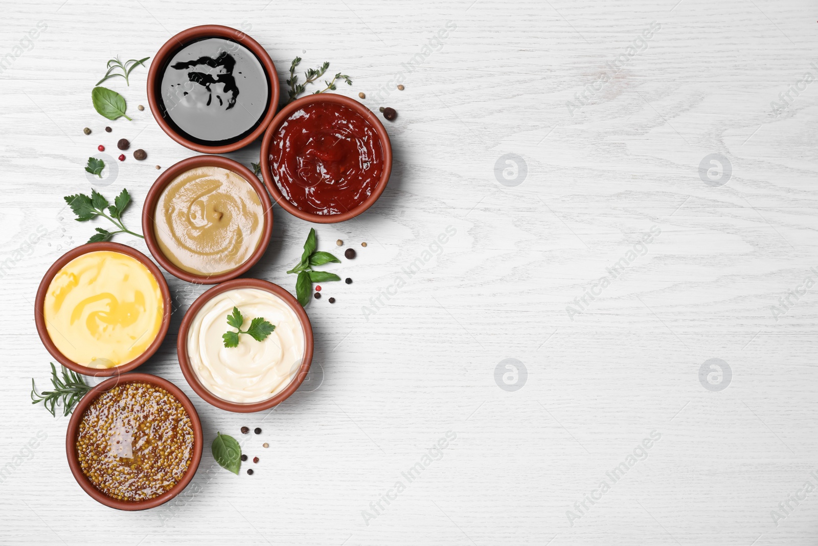 Photo of Many different sauces and herbs on white wooden table, flat lay. Space for text