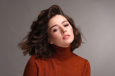 Portrait of beautiful young woman with wavy hairstyle on grey background