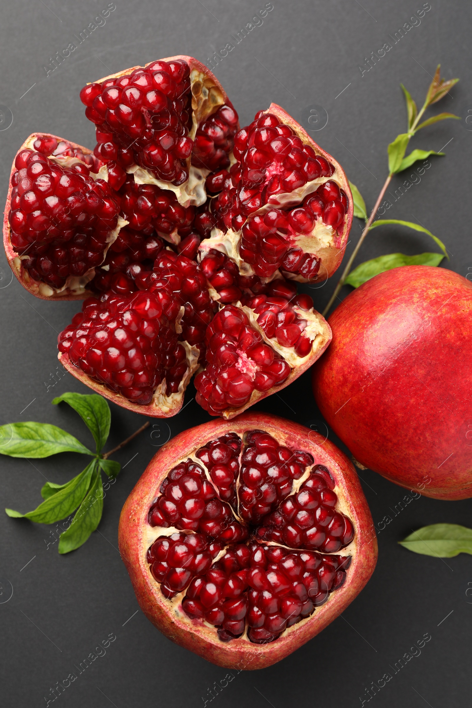 Photo of Fresh ripe pomegranates and leaves on grey background, top view