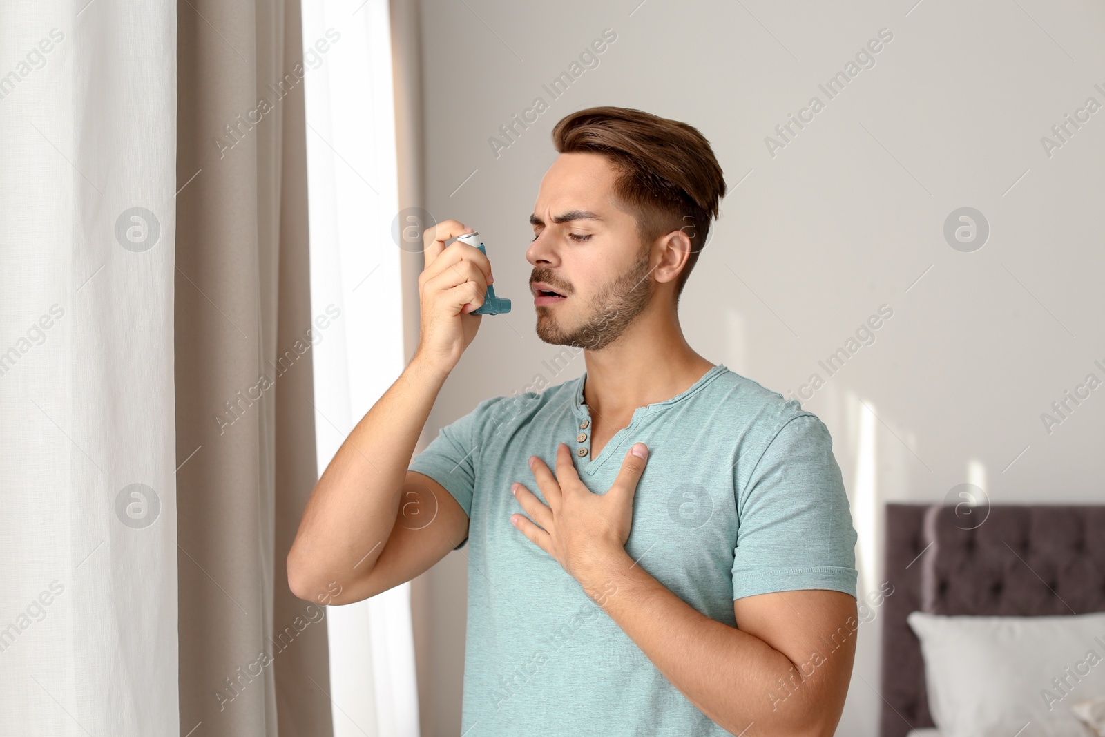 Photo of Young man using asthma inhaler at home