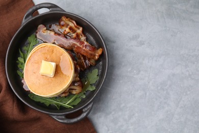 Photo of Tasty pancakes with butter, fried bacon and fresh arugula on grey table, top view. Space for text