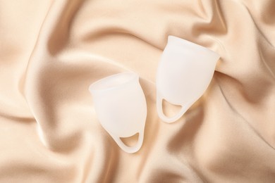 Photo of Menstrual cups on beige silk fabric, flat lay