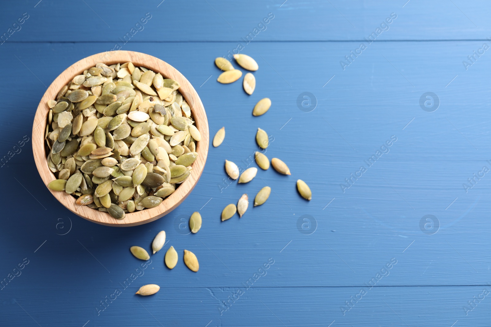 Photo of Bowl with peeled pumpkin seeds on blue wooden table, flat lay. Space for text