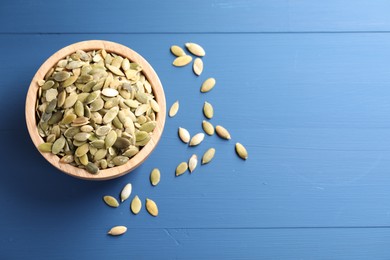 Bowl with peeled pumpkin seeds on blue wooden table, flat lay. Space for text