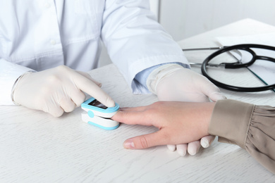 Doctor examining patient with fingertip pulse oximeter at white wooden table, closeup