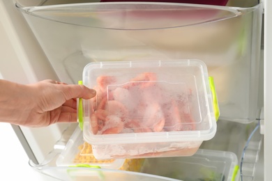 Woman taking container with frozen shrimps from refrigerator, closeup