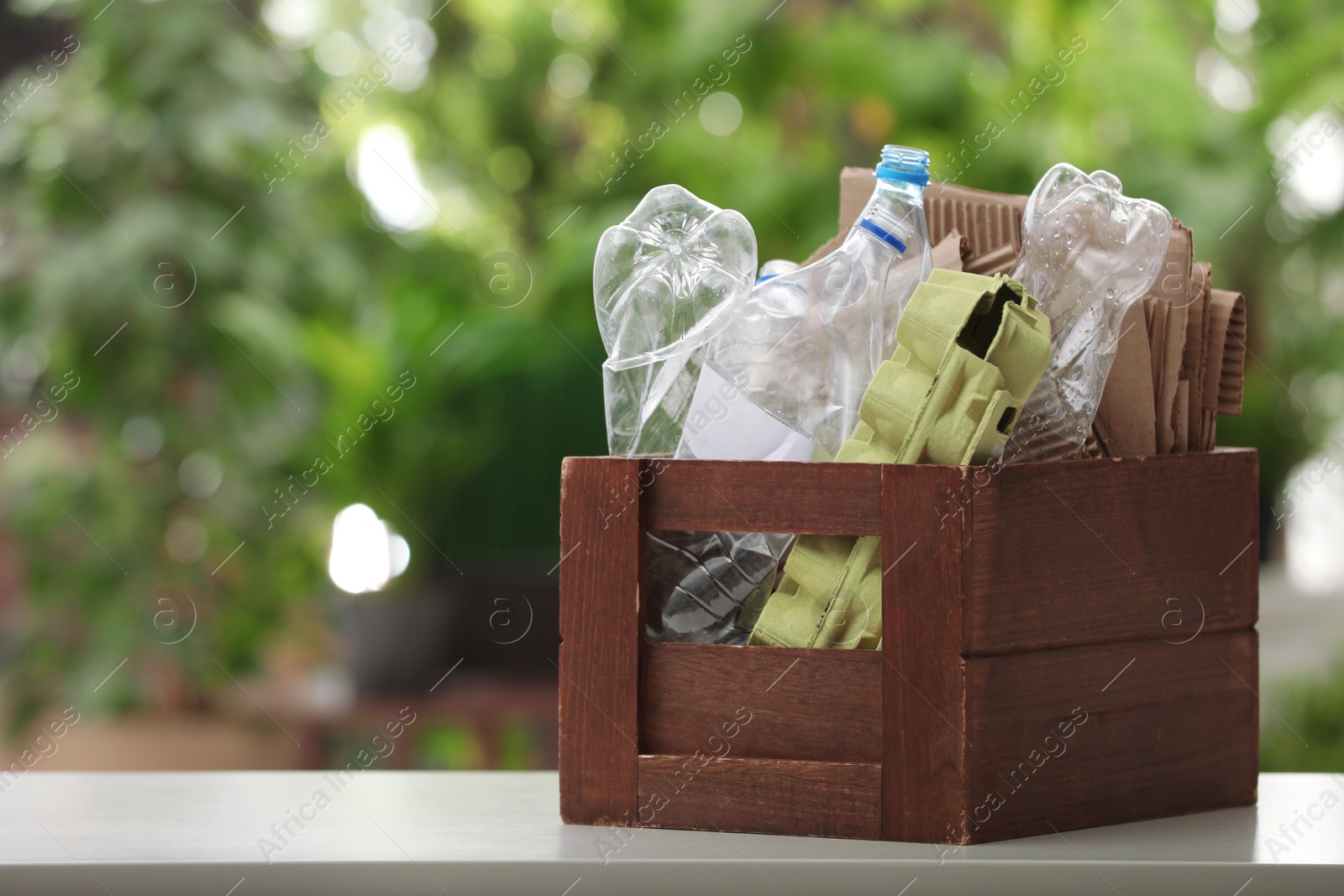 Photo of Wooden crate with different garbage on blurred background, space for text. Waste recycling concept