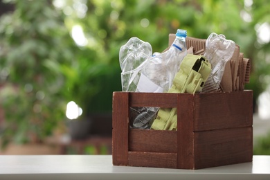 Photo of Wooden crate with different garbage on blurred background, space for text. Waste recycling concept