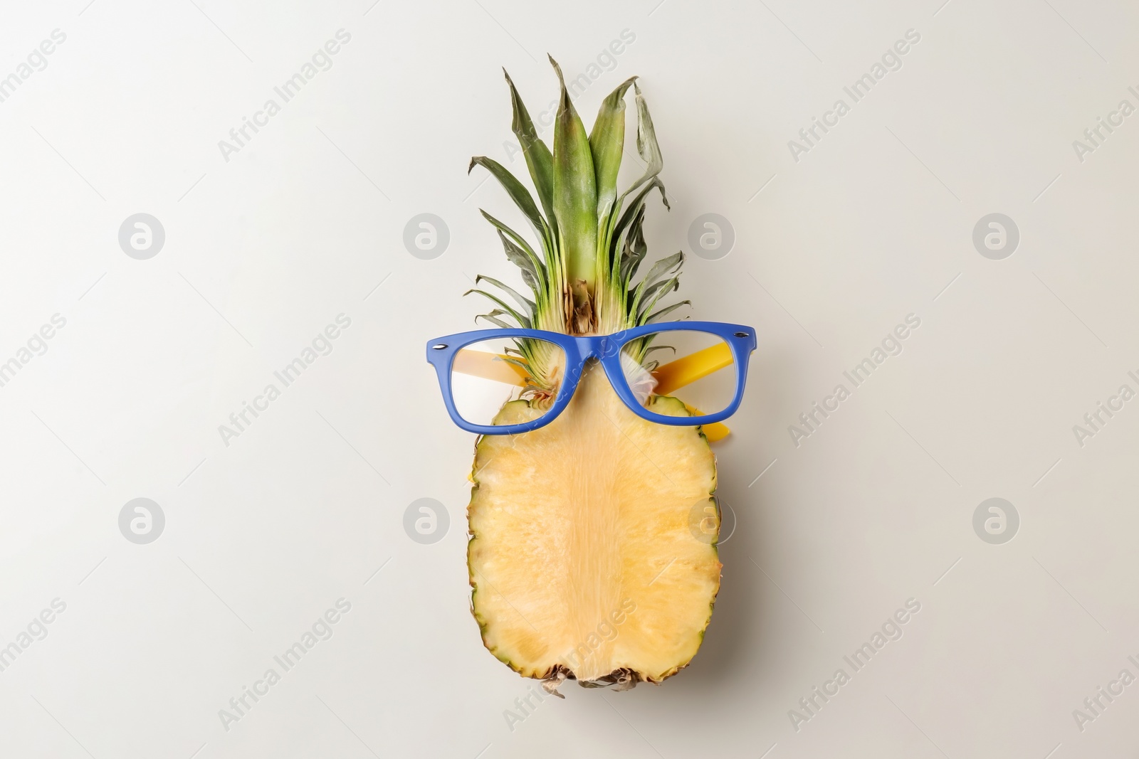 Photo of Funny cut pineapple with glasses on light background