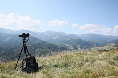 Photo of Tripod with modern camera and backpack in mountains on sunny day. Professional photography