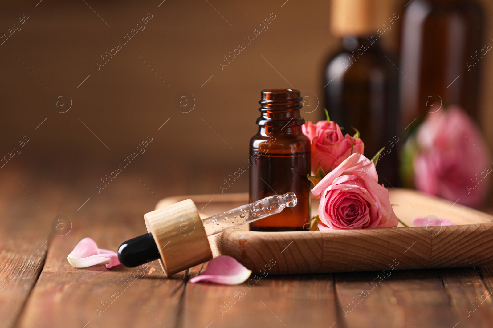 Photo of Bottle of essential rose oil and flowers on wooden table, space for text