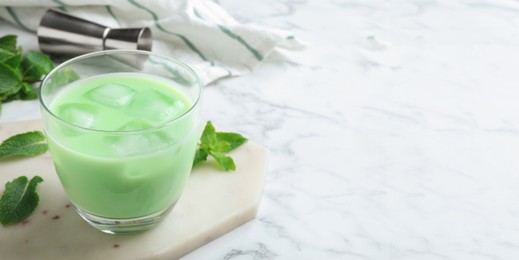 Image of Delicious mint liqueur with ice cubes and green leaves on white marble table, closeup with space for text. Banner design