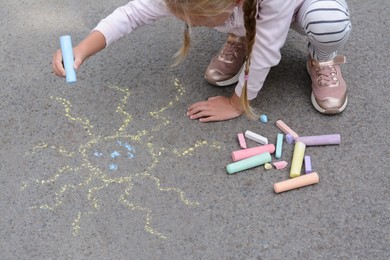 Little child drawing sun with chalk on asphalt, closeup