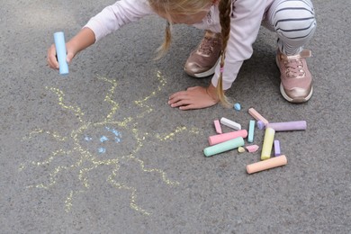 Photo of Little child drawing sun with chalk on asphalt, closeup