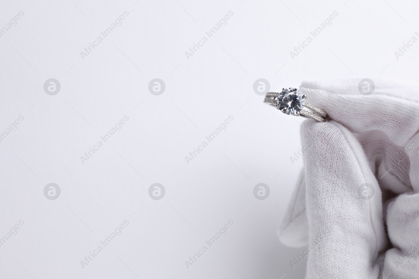 Photo of Jeweler holding diamond ring on white background, closeup. Space for text