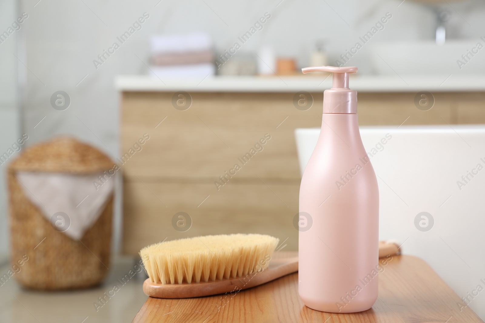 Photo of Bottle of shower gel and brush on wooden table near tub in bathroom, space for text