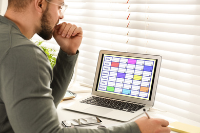 Young man using calendar app on laptop in office, closeup