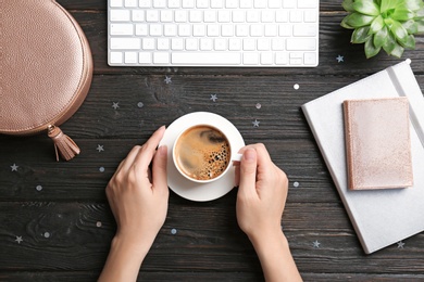 Photo of Young woman with cup of delicious hot coffee at table, top view