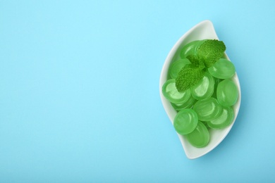 Photo of Plate with tasty mint candies and leaves on color background, top view