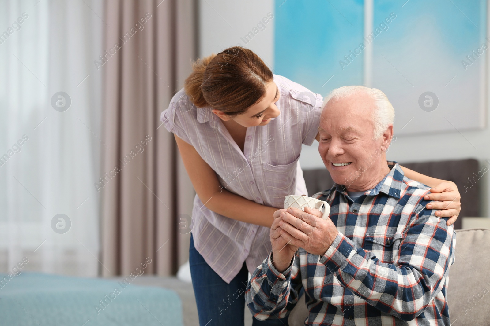 Photo of Elderly man with cup of tea near female caregiver at home. Space for text