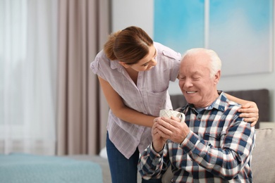 Elderly man with cup of tea near female caregiver at home. Space for text