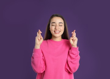 Woman with crossed fingers on purple background. Superstition concept