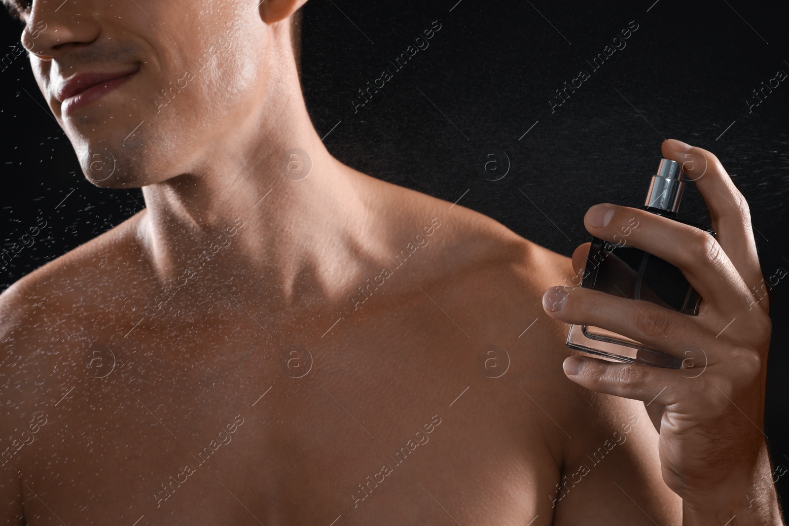 Photo of Young man using perfume on black background, closeup