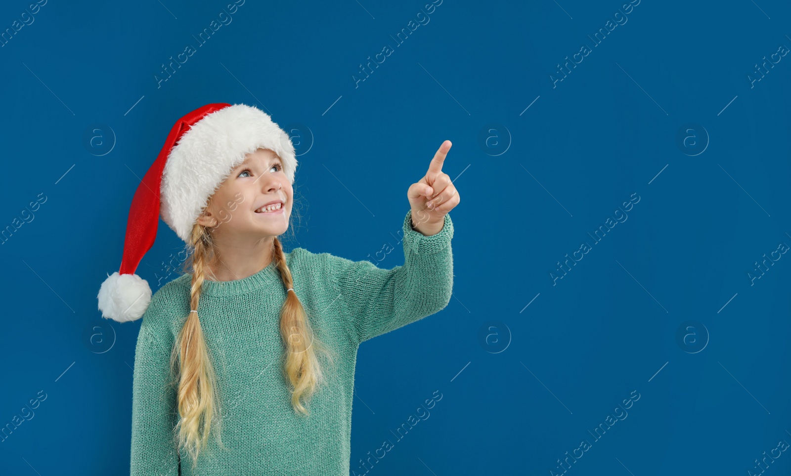 Photo of Cute little child wearing Santa hat on blue background. Christmas holiday