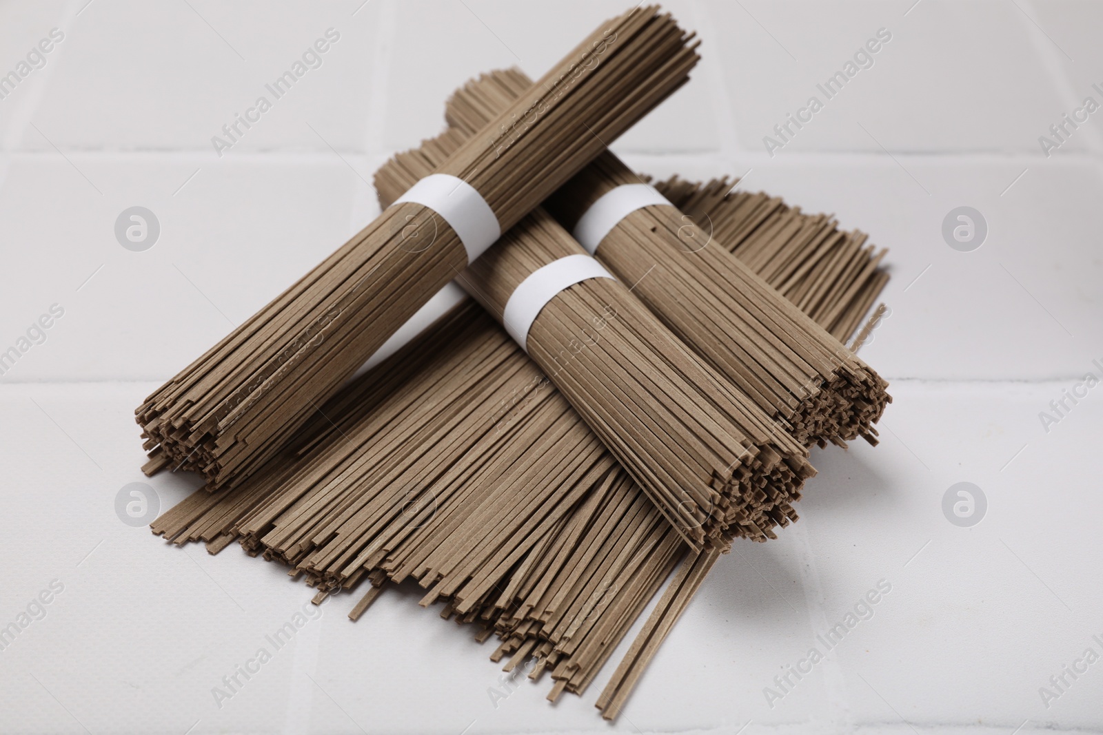 Photo of Uncooked buckwheat noodles (soba) on white tiled table, closeup