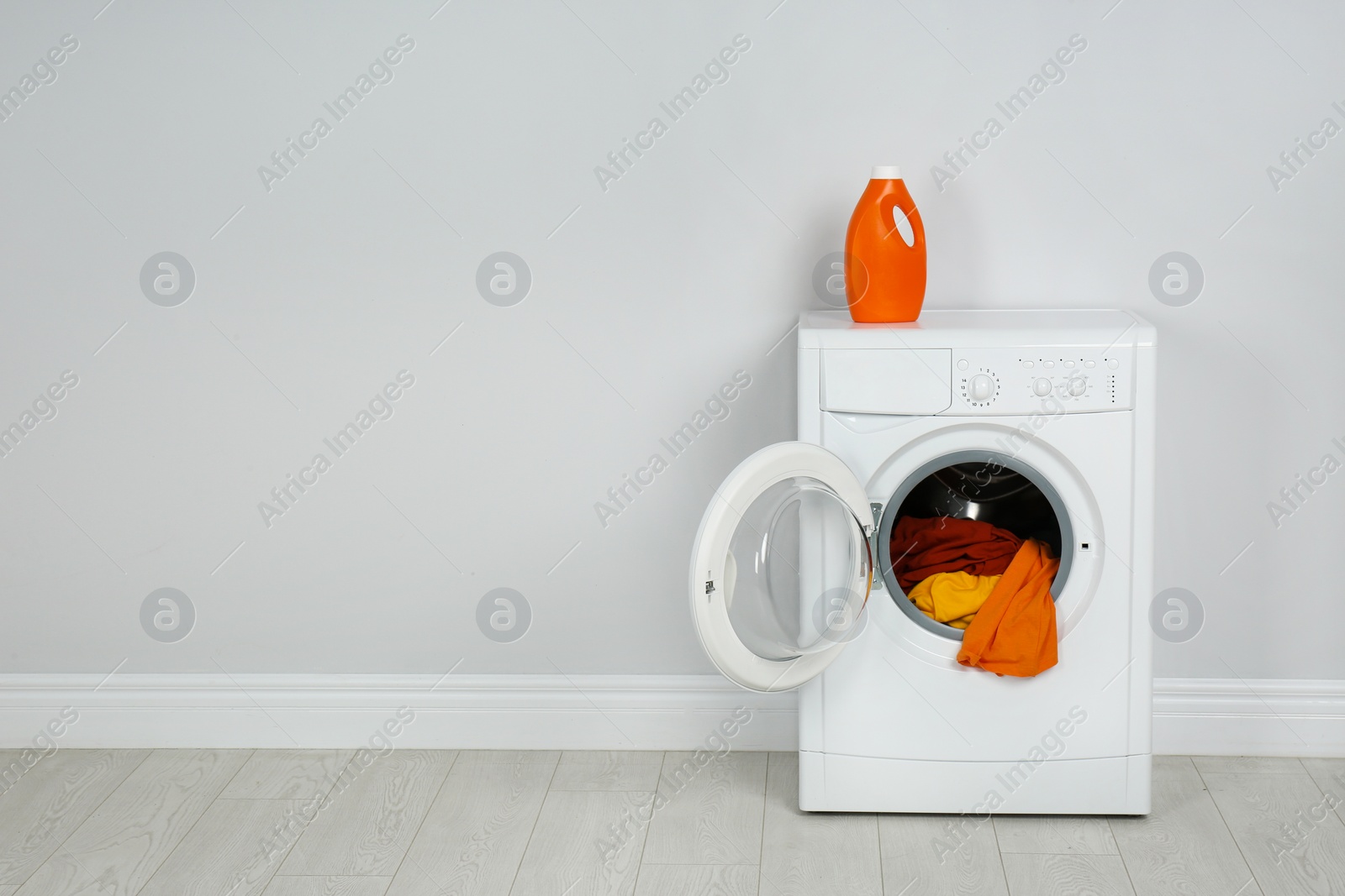 Photo of Modern washing machine with laundry and detergent near white wall. Space for text