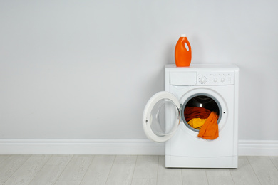 Modern washing machine with laundry and detergent near white wall. Space for text