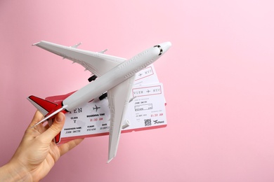 Photo of Woman holding toy airplane and tickets on pink background, closeup