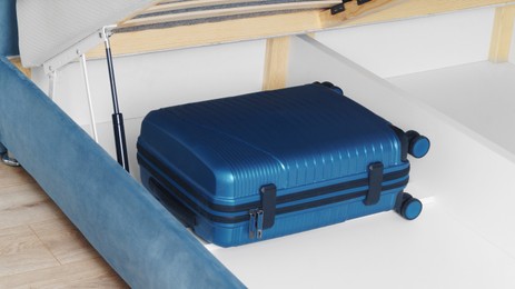 Photo of Storage drawer under bed with blue suitcase indoors