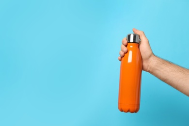 Photo of Man holding orange thermos bottle on light blue background, closeup. Space for text
